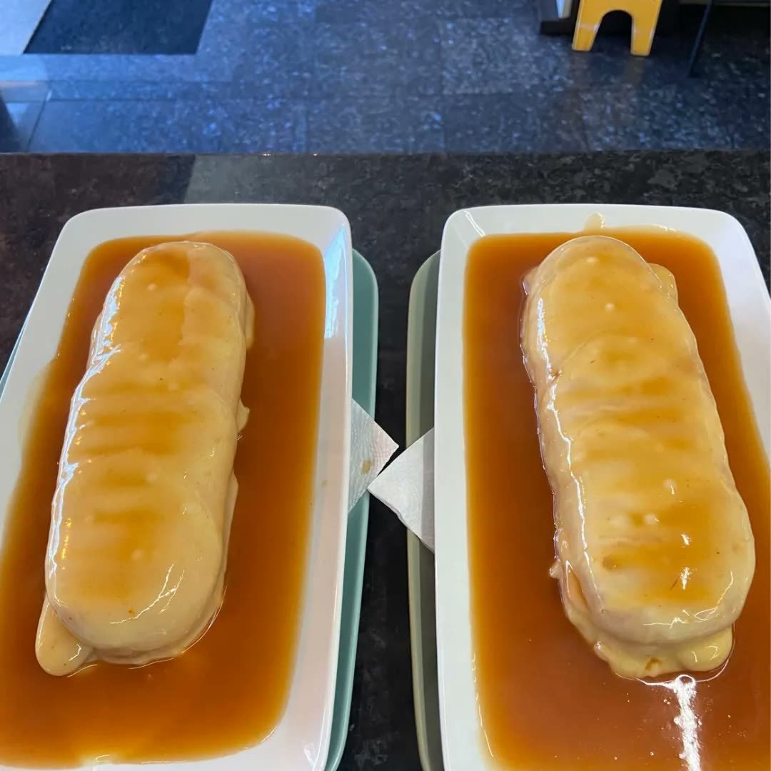 Zwei Spezial-Hotdogs in rechteckigen Schalen, mit Käse und Sauce bedeckt