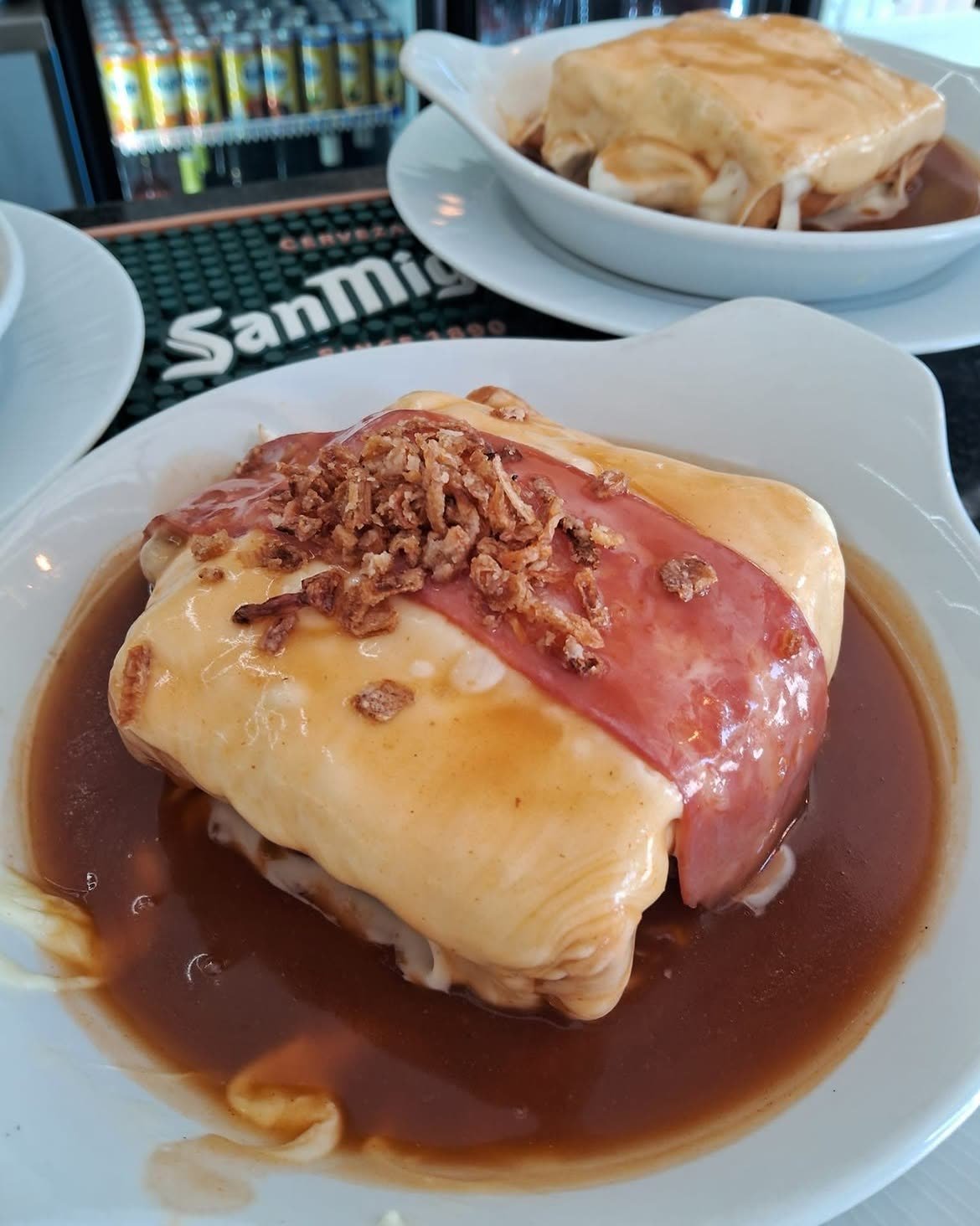 Zwei Francesinhas Capa Negra an der Theke, mit Sauce und gebratenen Zwiebeln bedeckt